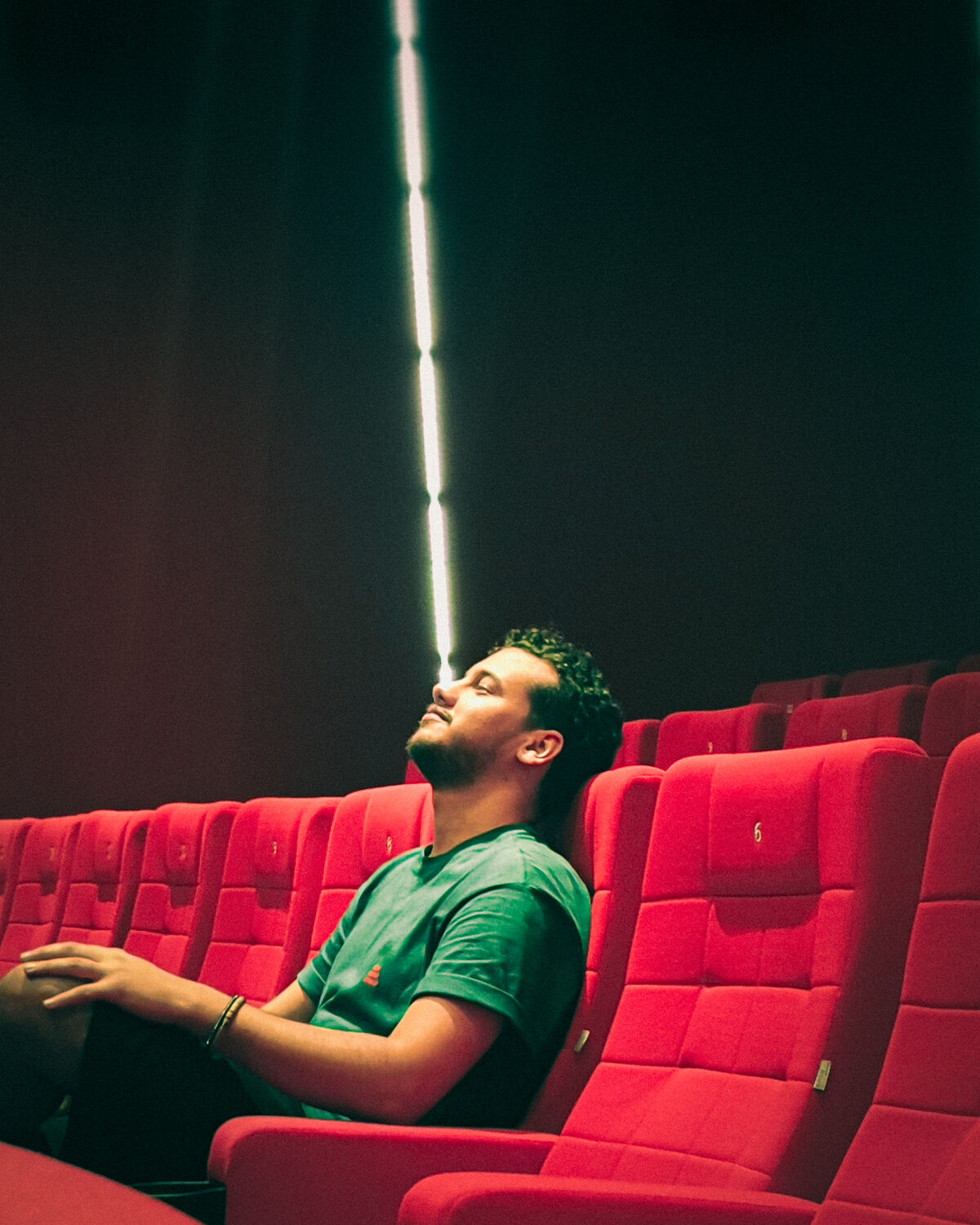 Mohammed in red cinema seats, eyes closed under a beam of light